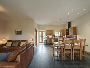 Ein modernes Wohnzimmer mit einer Ledersofa, einem Essbereich mit Holzsesseln und einem Tisch sowie einer Küche mit Holzschränken.