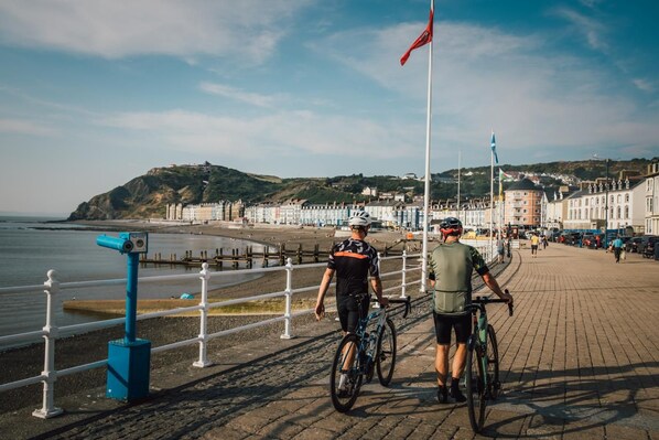 A coastal promenade with a beach, a flag, and buildings in the background. - 3 Bed in Talybont (oc-b46034) (Llandre)