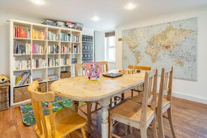 Ein Zimmer mit einem Holztisch, Stühlen, einem Bücherregal, einer Weltkarte und Kinderspielzeug.