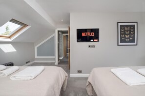 A hotel room with two beds, a TV mounted on the wall, and a skylight. - 7 Bed in Earswick (oc-s46053) (Earswick)