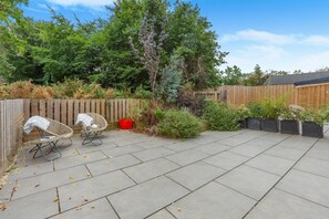 Eine Terrasse mit Holzzaun, zwei Korbstühlen und einem roten Blumentopf.