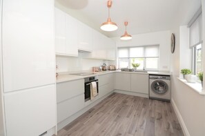 Une cuisine moderne avec des armoires blanches, un four encastré, un lave-linge et des luminaires suspendus.