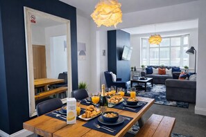 Ein Essbereich mit einem Holztisch, gedeckt für das Frühstück, ein Spiegel und ein Wohnzimmer mit einer Couch und einem Fernseher.