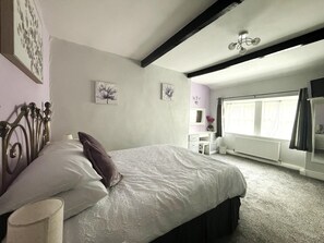 Ein Schlafzimmer mit einem Bett, einem Schminktisch, einem Heizkörper und einem Fenster mit Vorhängen.