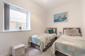 A bedroom with two beds, a window with blinds, a small bedside table with a lamp, and a painting on the wall. - 2 Bed in Bournemouth (oc-s45959) (Christchurch)