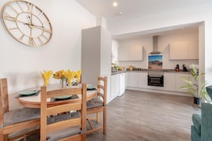 A modern kitchen with white cabinets, a built-in oven, and a dining area with a wooden table and chairs. - 2 Bed in Bournemouth (oc-s45959) (Christchurch)