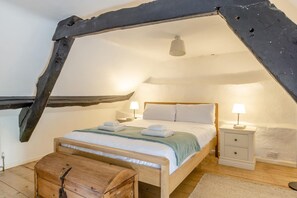 Un dormitorio con techo inclinado, una cama de madera, dos mesitas de noche con lámparas y un pequeño cofre de madera.
