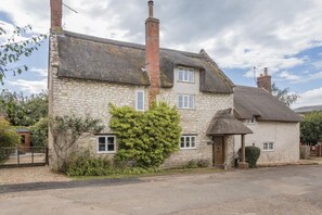 A stone house with a thatched roof, a chimney, and a small garden. - 3 Bed in Bridport (oc-f45448) (Bothenhampton)