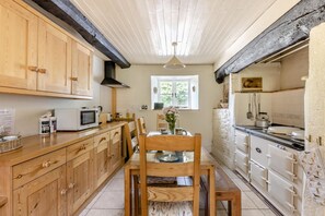 A kitchen with wooden cabinets, a dining table with chairs, a microwave, and a stove. - 3 Bed in Bridport (oc-f45448) (Bothenhampton)