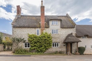 A stone house with a thatched roof, a chimney, and a small door. - 3 Bed in Bridport (oc-f45448) (Bothenhampton)