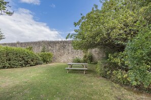 A grassy area with a picnic table, a stone wall, and dense foliage. - 3 Bed in Bridport (oc-f45448) (Bothenhampton)