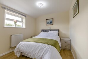 Une chambre à coucher avec un lit, une table de chevet, un tiroir, un radiateur, une fenêtre donnant sur un beau paysage et un tableau encadré accroché au mur.