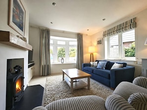 A living room with a fireplace, sofa, coffee table, and a view of the outdoors through large windows. - 3 Bed in Thornham (oc-h45956) (Thornham)