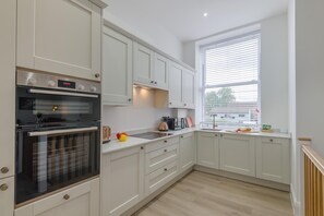 A modern kitchen with white cabinetry, a built-in oven, and a window with blinds. - 2 Bed in Chipping Sodbury (oc-r45995) (Chipping Sodbury)
