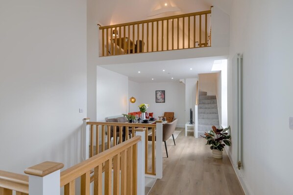 En rummelig indretning med en trætrappe, et spiseområde med bord og stole, samt udsigt til en trappe, der fører op til en etage over.