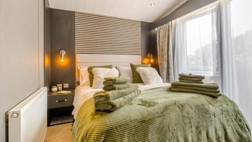 A hotel room with a bed, a nightstand, a window with curtains, and a radiator.