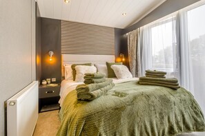 A hotel room with a bed, a nightstand, a window with curtains, and a radiator.