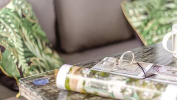 Une table en verre sur laquelle se trouvent un magazine enroulé, une paire de lunettes et un objet bleu.