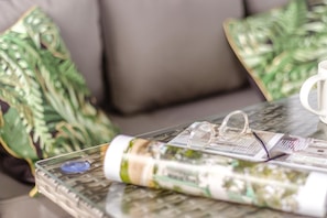 A glass table with a rolled-up magazine, a pair of glasses, and a blue object on it.