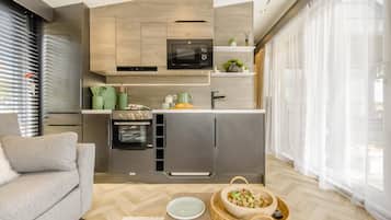 Une cuisine moderne dotée d’appareils électroménagers intégrés, un coin repas avec un canapé et une grande fenêtre agrémentée de rideaux légers.