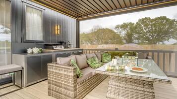 Une cuisine extérieure moderne dotée d’un barbecue intégré, d’un coin salon avec un canapé confortable et des meubles en osier, ainsi que d’une table en verre pour les repas en plein air.