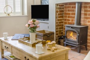 A cozy living room with a fireplace, a television, and a wooden coffee table with decorative items. - 1 Bed in Holt (oc-a46046) (Holt)