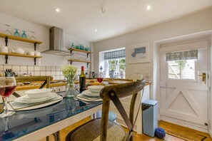 A modern kitchen with a dining table set for two, a wine glass, and a vase with flowers. - 1 Bed in Holt (oc-a46046) (Holt)
