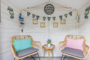 A cozy porch with two wicker chairs, a small table with a plant, and a 'Welcome to the Summer House' sign. - 1 Bed in Holt (oc-a46046) (Holt)