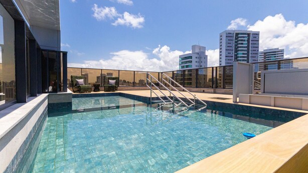 Una piscina sul tetto con barriera in vetro, scala in metallo e vista sulla città.