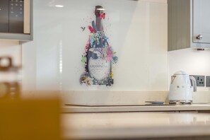 Et køkken med en hvid bordplade, en hvid elkedel og en dekorativ vægkunst af en champagneflaske.