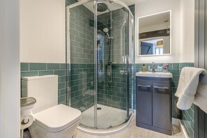 Uma casa de banho moderna com chuveiro envidraçado, sanita branca e lavatório com espelho.