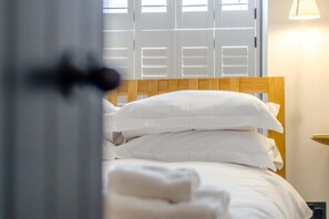 Ein Bett mit weißer Bettwäsche und einem Holz-Kopfteil in einem Zimmer mit Fenster und Lampe.