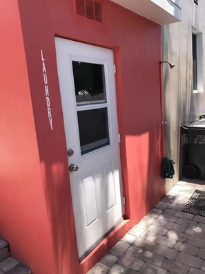 Ein rotes Gebäude mit einer weißen Tür und einem Fenster, einer Metall-Türklinke und einem kleinen Lüftungsgitter über der Tür.