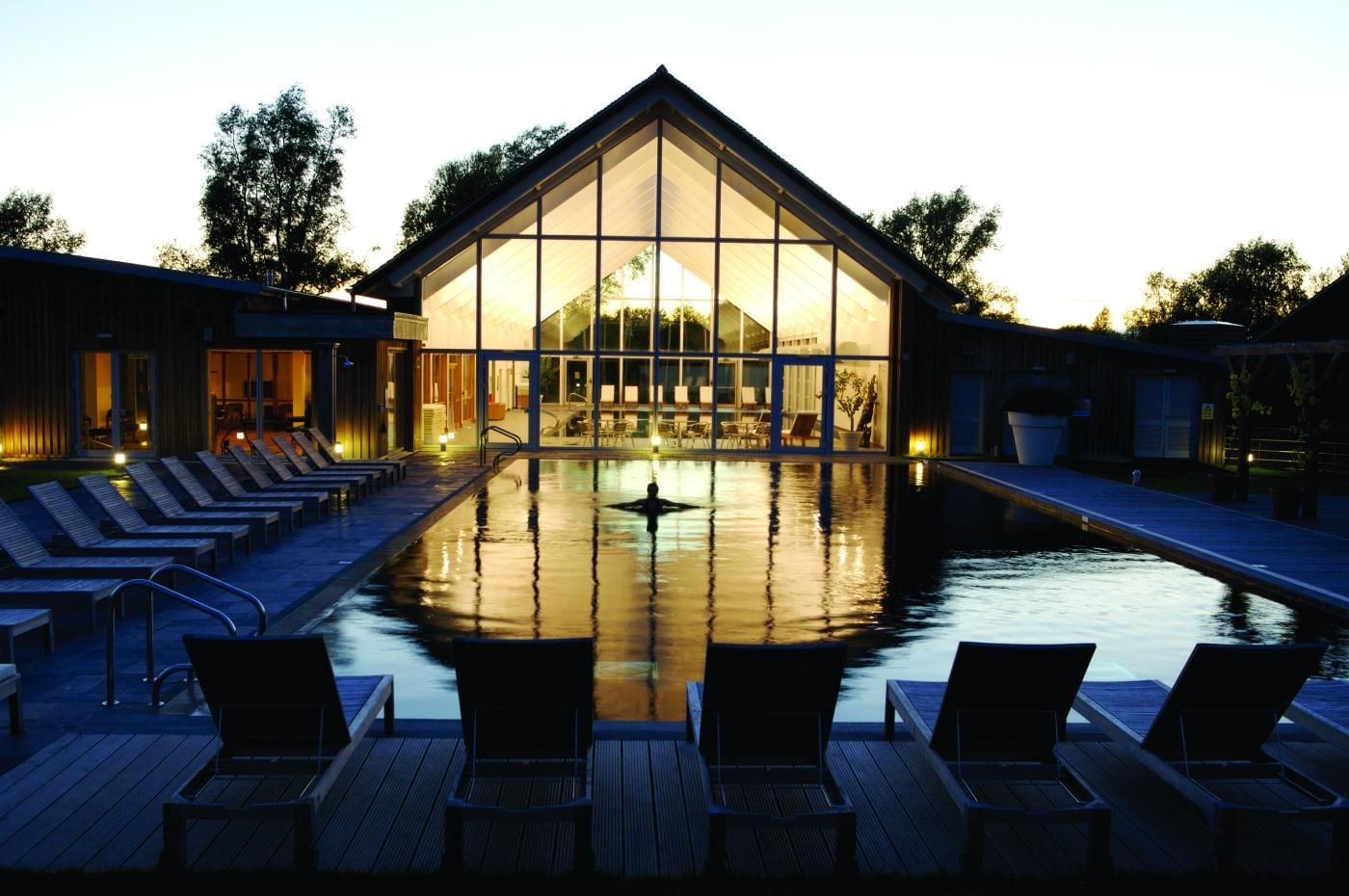 A modern building with a glass facade, a swimming pool, and lounge chairs.