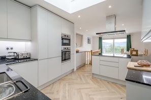 A modern kitchen with white cabinets, a toaster, an oven, and a window with a view. - 5 Bed in Keswick (oc-m46014) (Keswick)