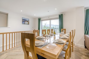 A dining room with a long table set for a meal, wooden chairs, a window with a view, and a painting on the wall. - 5 Bed in Keswick (oc-m46014) (Keswick)