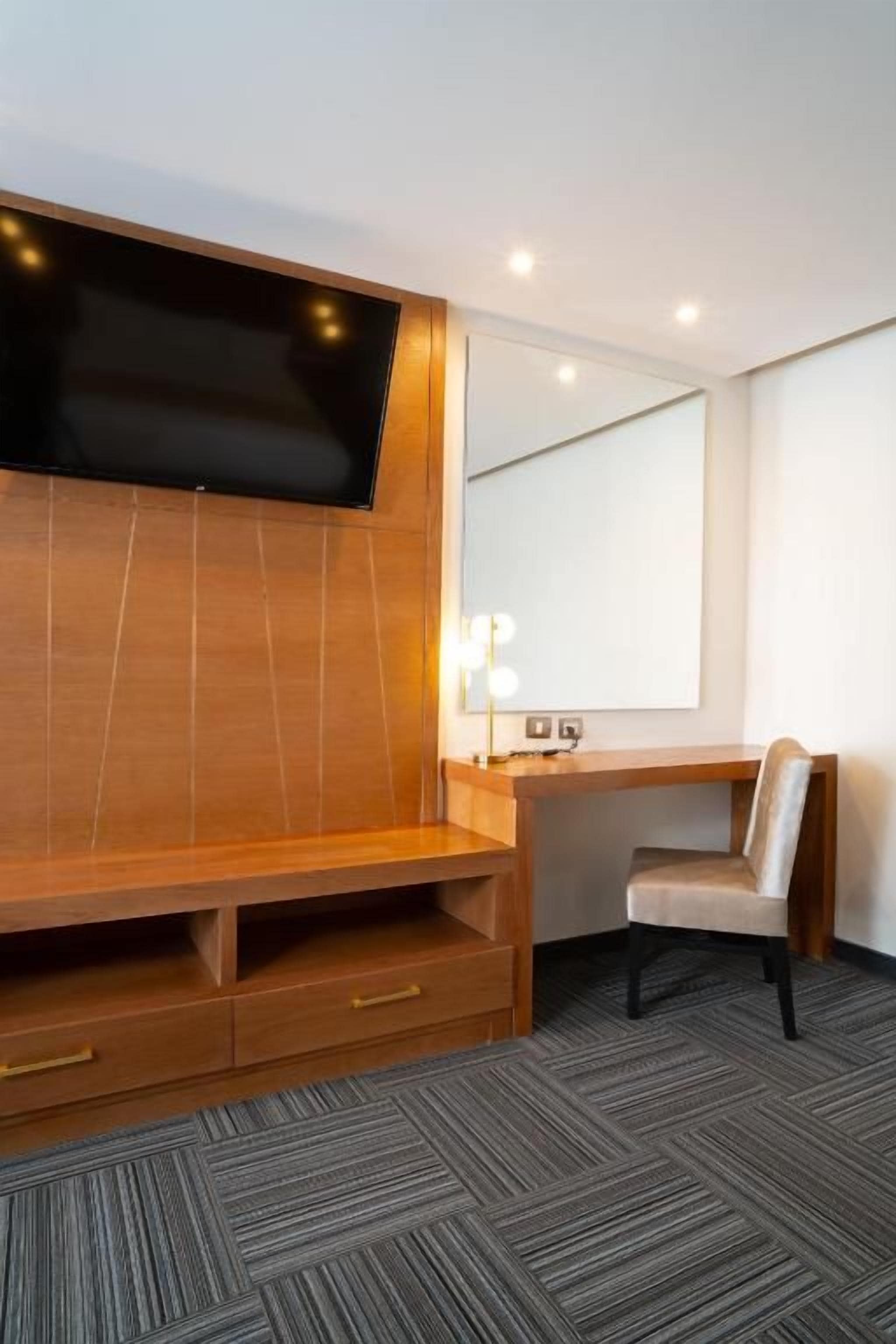 Ein Hotelzimmer mit einer Holztrennwand, einem Schreibtisch mit Stuhl, einem großen Spiegel und einem Teppichboden.