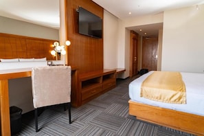 Habitación de hotel con cama, escritorio, silla, televisor y espejo con iluminación.
