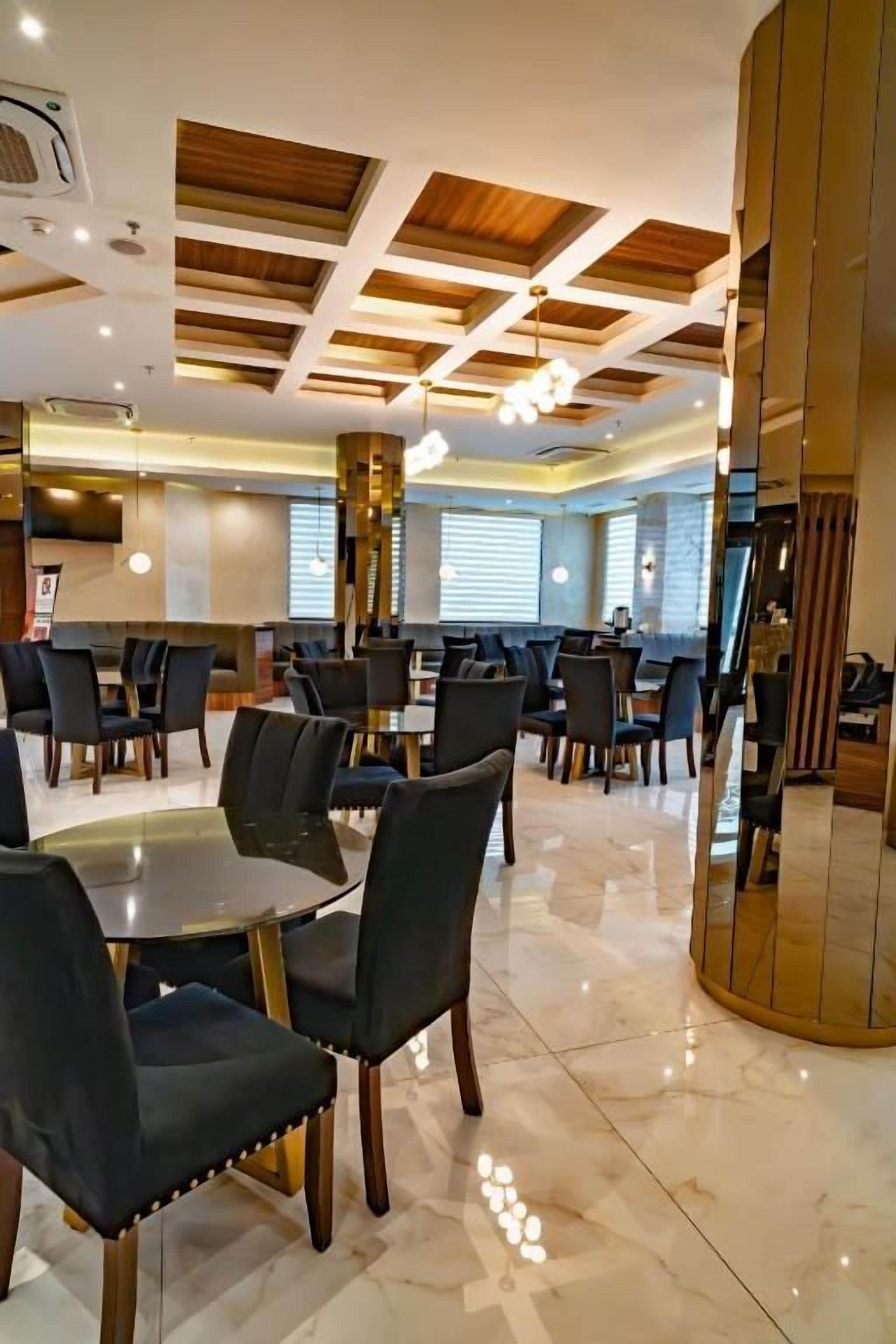 A modern dining area with round tables and chairs, a polished floor, and a wooden ceiling with recessed lighting.