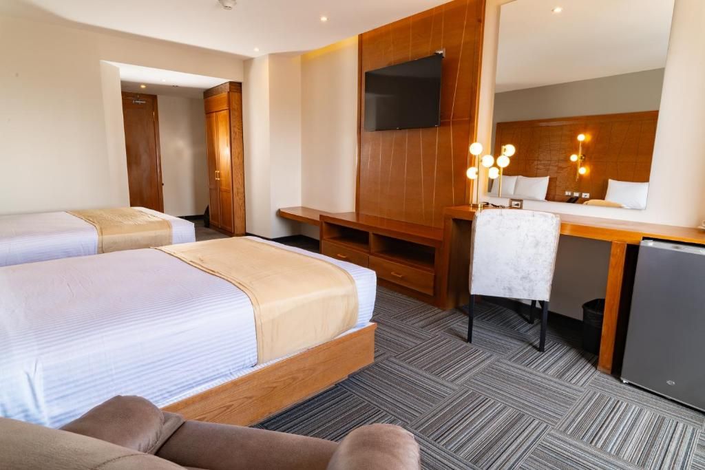 Une chambre d’hôtel avec deux lits, un bureau, une télévision et un miroir.