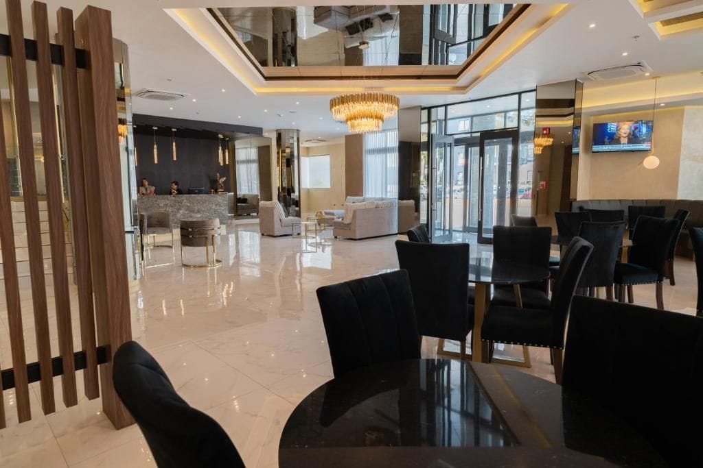 A modern hotel lobby with a reception desk, seating area, and a large chandelier.