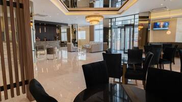 A modern hotel lobby with a reception desk, seating area, and a large chandelier.