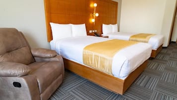A hotel room with two beds, a sofa, and a wooden headboard with wall-mounted lights.