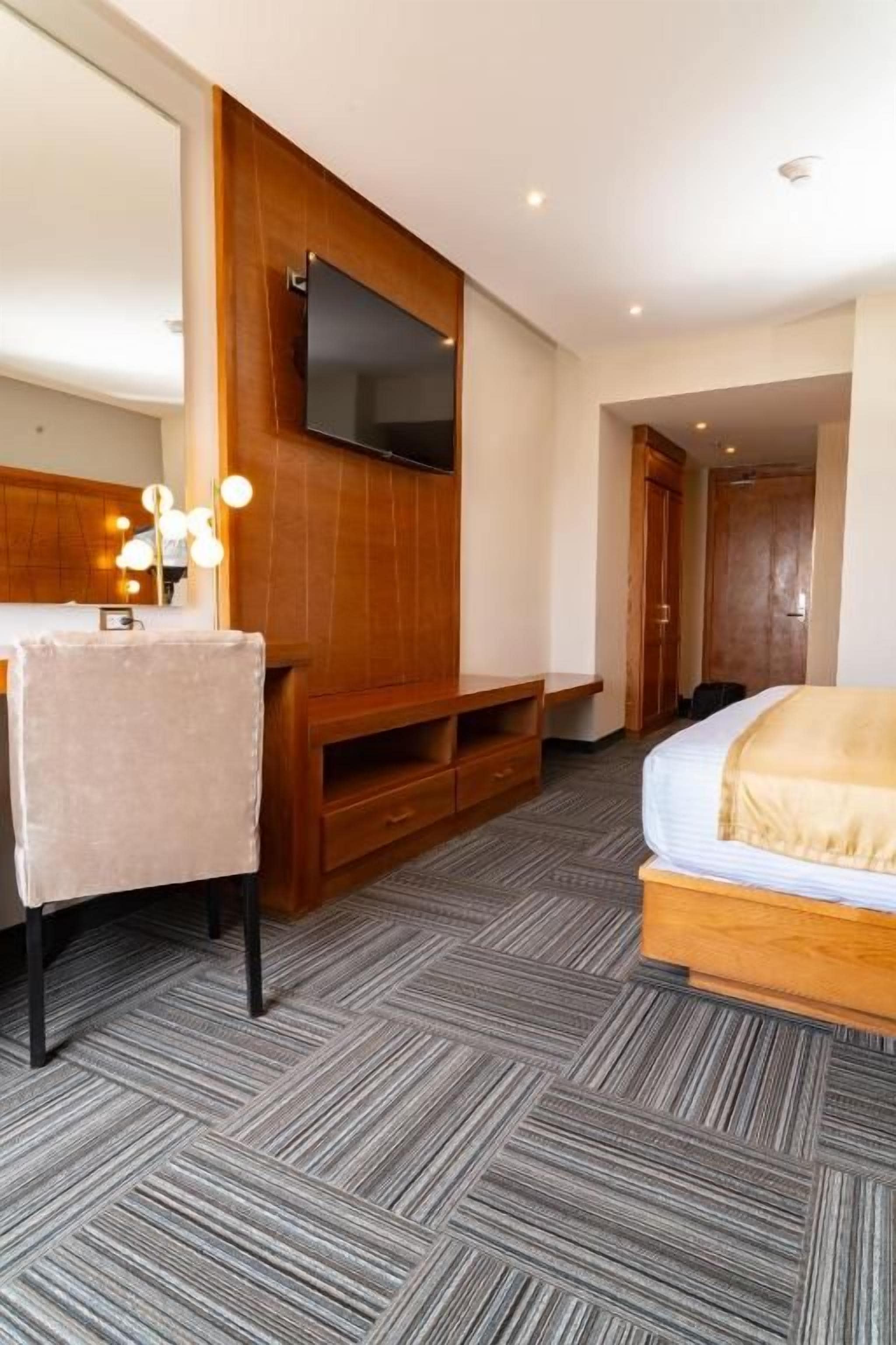 A hotel room with a bed, a TV mounted on the wall, a wooden bench, and a carpeted floor.