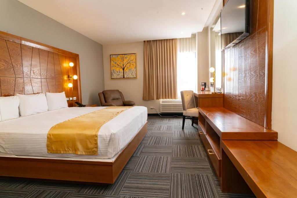 A hotel room with a large bed, a desk, a chair, a television, and a painting on the wall.