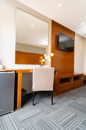 Habitación de hotel compacta con kitchenette, un televisor de pantalla plana en la pared, un escritorio de madera y una silla.