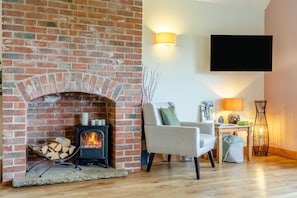 A living room with a brick fireplace, a sofa, a television mounted on the wall, and a floor lamp. - 3 Bed in Yoxall (oc-s46074) (Hadley End)