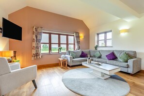 Ein Wohnzimmer mit einer Couch, einem Sessel, einem Couchtisch und einem an der Wand befestigten Flachbildfernseher.