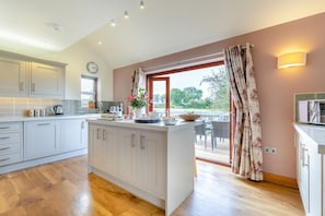 A kitchen with a central island, wooden flooring, and a view to an outdoor deck. - 3 Bed in Yoxall (oc-s46074) (Hadley End)