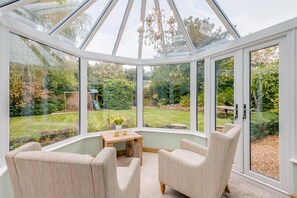 A conservatory with a glass roof, a wooden table with flowers, and two upholstered chairs. - 5 Bed in Potto (oc-t46322) (Potto)